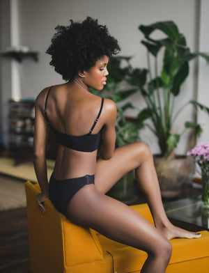Slick Chicks - Adaptive AND sexy! Slick Chicks Ambassador Rissa is wearing  the Velcro Front Fastening Bra and High Waist Panty in black.  @fibrogirlblog . ID: A woman standing against a white